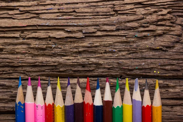 Row of colored drawing pencils on grunge natural wooden background