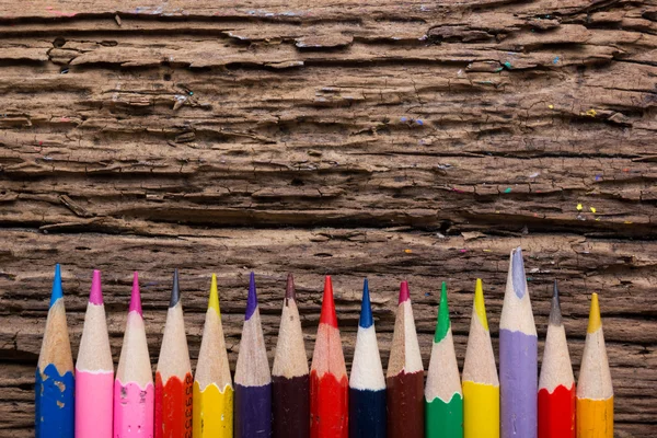 Row of colored drawing pencils on grunge natural wooden background