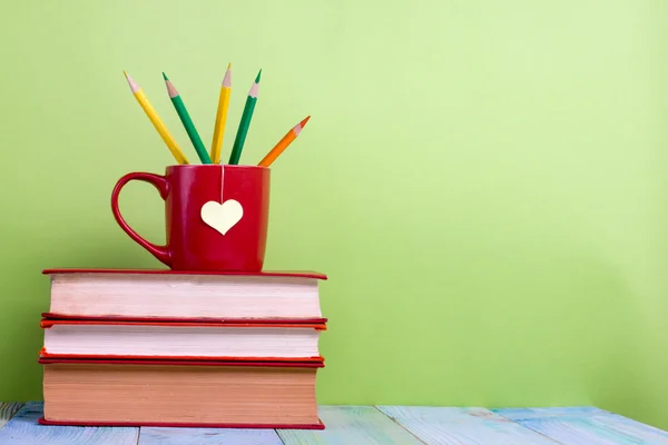 Back to school. Composition with old vintage hardback books and red cup, heart, pencils