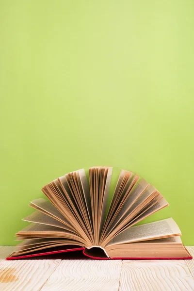 Open hardback book, diary with fanned pages on green background and wooden deck table. Back to school.