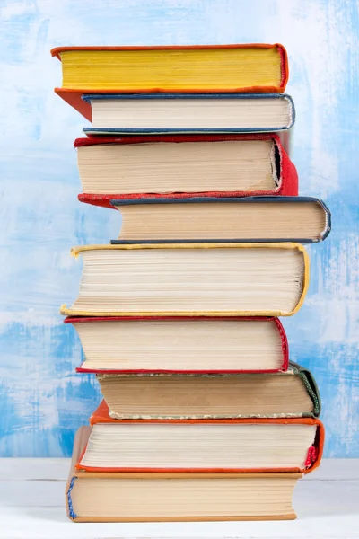 Composition with old vintage colorful hardback books, diary on wooden deck table and artistic blue background