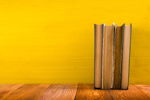 Row of colorful hardback books on yellow background.