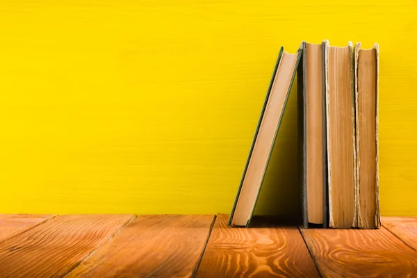 Row of colorful hardback books on yellow background.