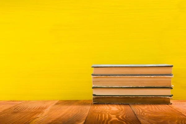 Stack of colorful hardback books on yellow background.