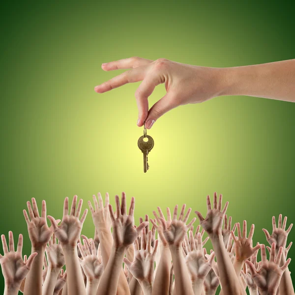 REAL ESTATE concept. Many hands want to get the key, reaching out for key - concept of winning a house, apartment. Close up view of hand holding key to a dream house. Clipping pass and copy space. Green background
