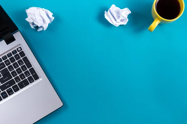 Office table desk with set of colorful supplies, white blank note pad, cup, pen, pc, crumpled paper, flower on blue background. Top view and copy space for text