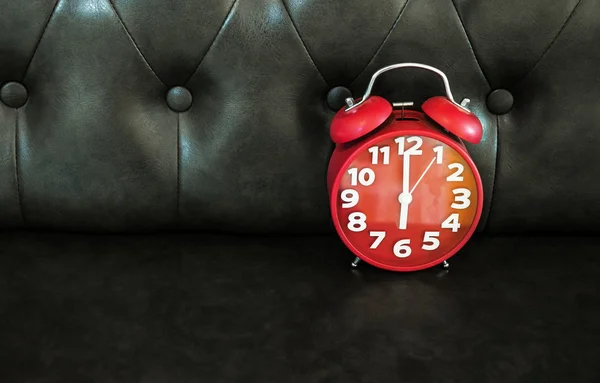 Red retro alarm clock on dark sofa.