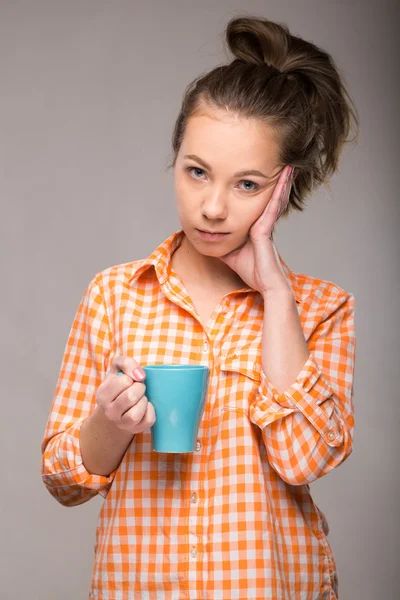 Studio portrait of a sleepy woman in an orange shirt with a cup