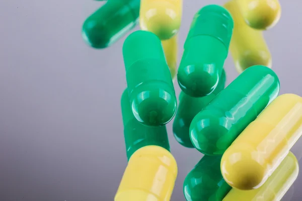 Yellow and green capsules medications on a mirrored background