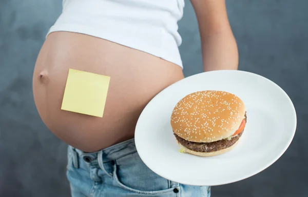 Close up of a cute pregnant belly and junk food. Hamburger and p