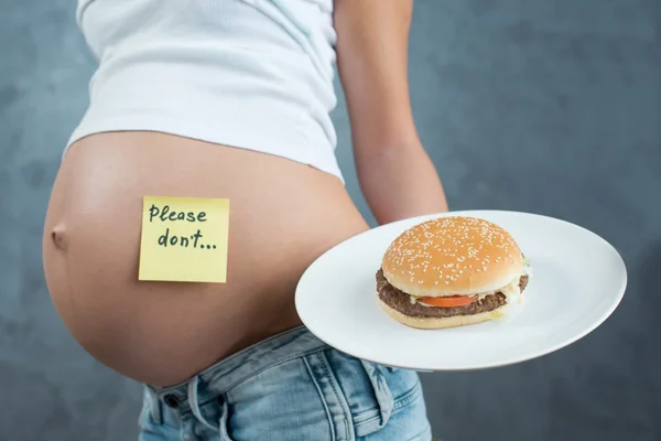Close up of a cute pregnant belly and junk food. Hamburger and p