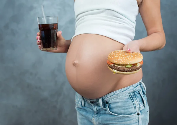 Close up of a cute pregnant belly and junk food. Hamburger and p