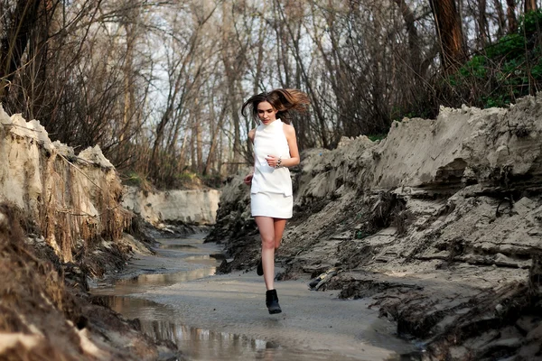 Girl in white short dress runs on sand