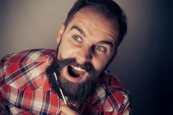 Young man comb his beard and moustache on gray background