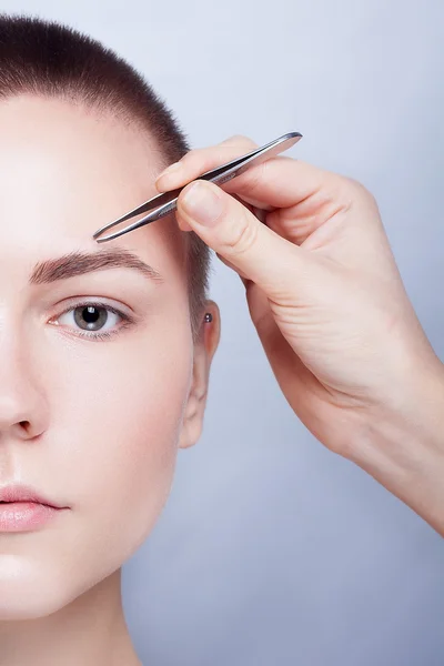Young woman with short hair plucking eyebrows tweezers close up