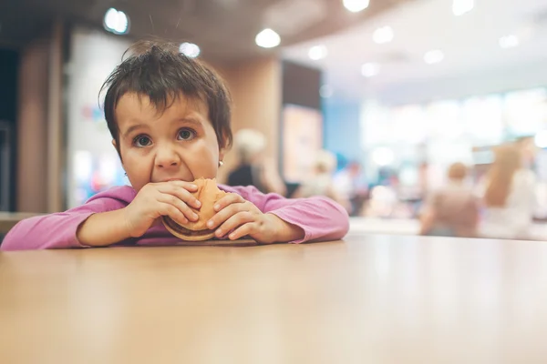 Cute little Latin girl eating a hamburger and looking up towards copy space