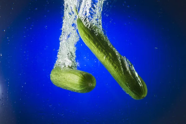 Two green cucumber in water on a blue background