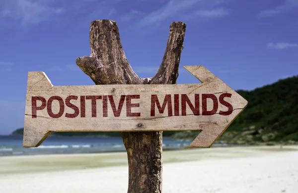 Positive Minds wooden sign with a beach on background