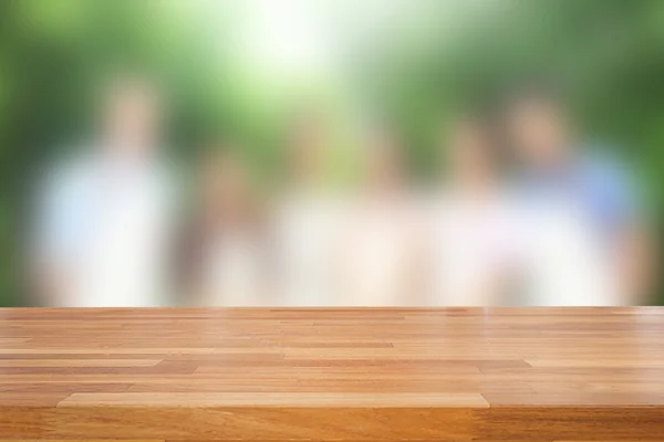 Empty wooden table against group of people with tree background