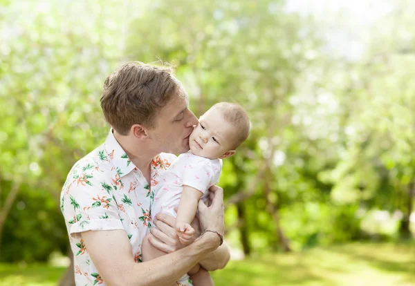 Father kissing his cute baby  outdoors in spring park against na