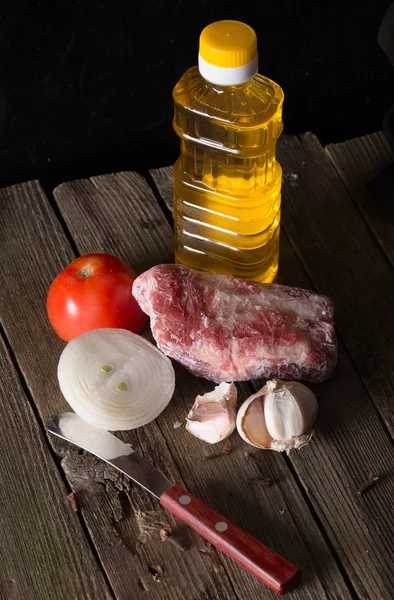 Piece of the frozen meat, vegetables and oil on a wooden table