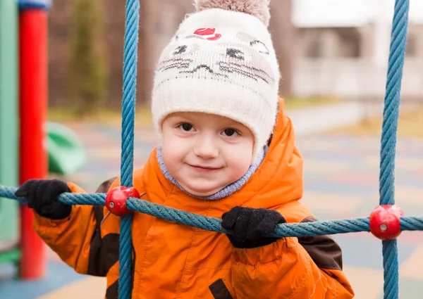 The kid at a playground holds a rope ladder in the fall