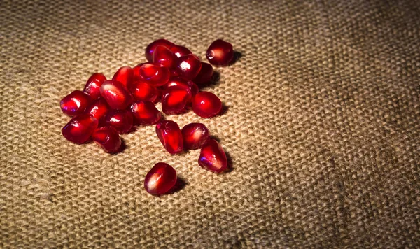 Some ripe red grains of pomegranate are scattered on a sacking