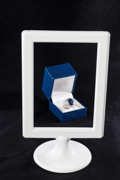Box of ring behind white frame on black background
