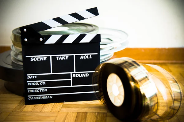 Movie clapper board and 35 mm film reel on wooden floor