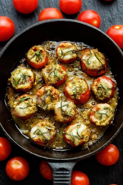 Roasted cherry tomatoes stuffed with herb pesto and mozzarella cheese on a cast-iron frying pan