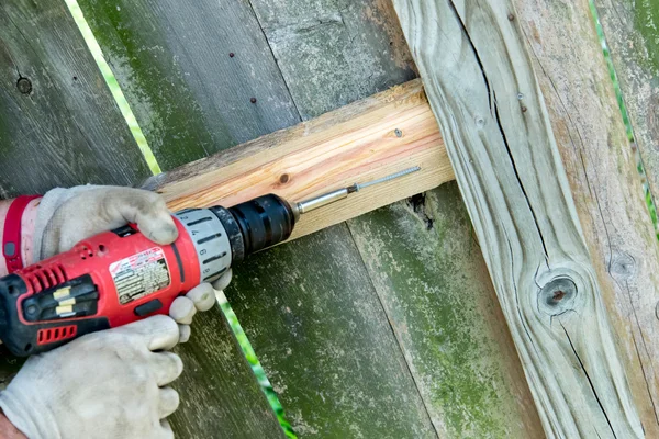 Man drilling holes for wood fence repair