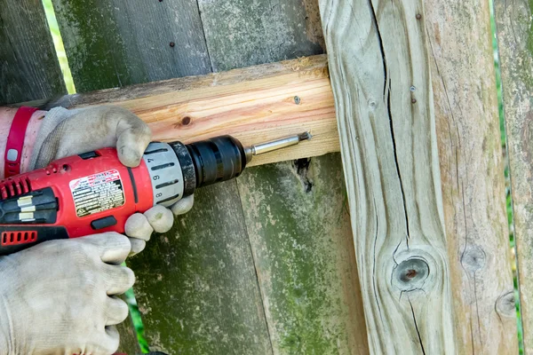 Man drilling holes for wood fence repair