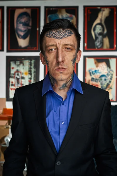 Tattooed man in black jacket and blue shirt in studio
