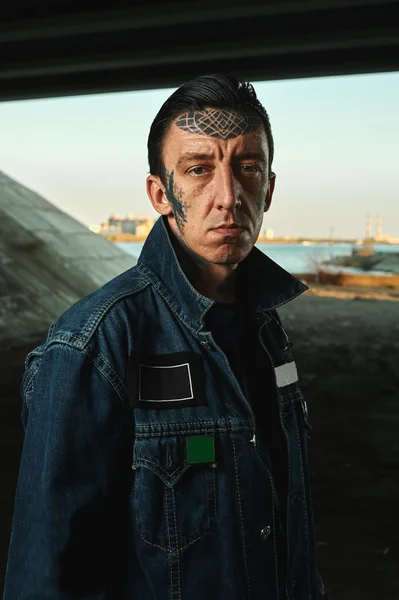 Outdoor Portrait of Man with tattooed Face in denim Jacket