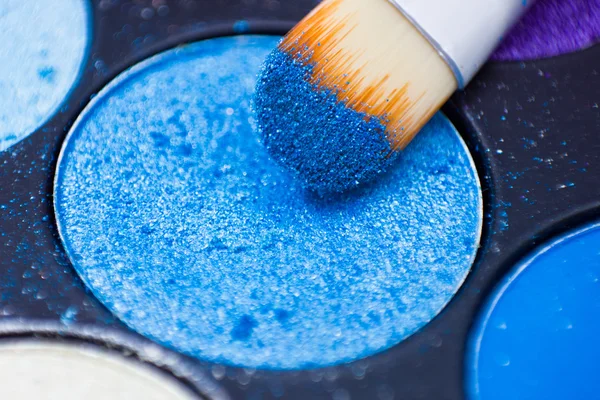 Brushes for make-up on the eye shadow palettes. Texture of crumbly  blue sparkling shadows.