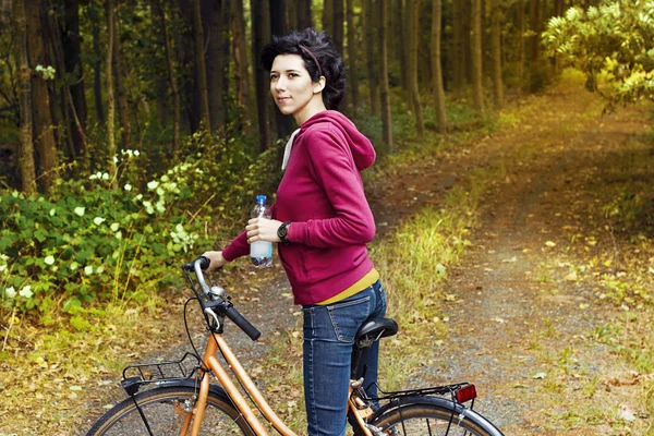 Young beautiful girl on a bicycle with a bottle of water in hand in the woods. Walking on a bicycle in the forest. A slim woman with a sports body shape on a bicycle.