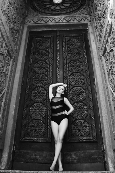 Portrait of a lovely young slim girl in a black bathing suit on a background Gothic building. Portrait of a fashion model.