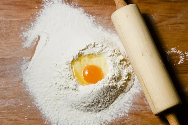 Ingredients for cooking dough on a wooden table. Flour, egg and a rolling pin.