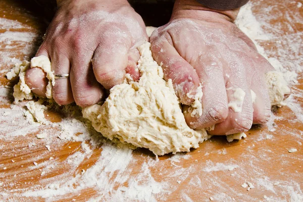 Men\'s hands knead the dough on the wooden table. The chef prepares the dough for Italian cuisine.