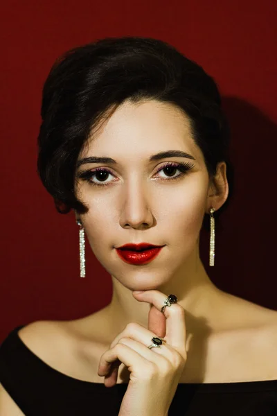 Portrait of a beautiful young girl in the jewelry on a red background. Elegant woman in diamond earrings and rings.