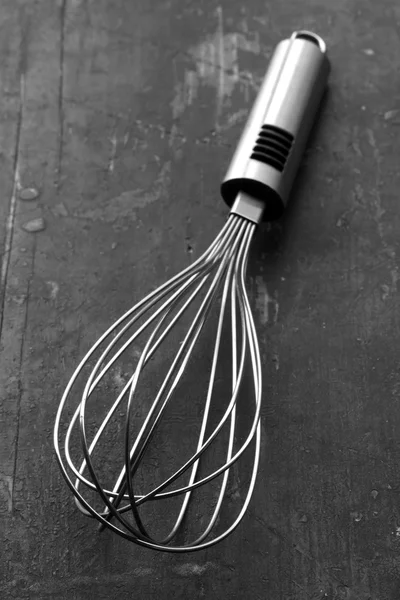 Steel kitchen whisk on an old black table closeup selective focus. rustic style. black and white photo