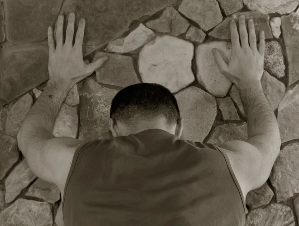 White man standing with his back having rested hands against a wall of stone. black and white toning, shallow depth of field. the concept of police searches, arrest