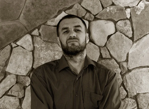 Portrait of grinning unshaven white man in a striped shirt against the wall of stone. black and white photo