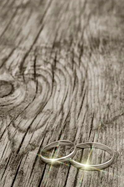 Male and female wedding rings in gold with multicolor glare on an old cracked wooden board. selective focus