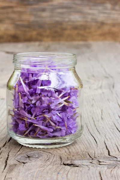 Pale lilac flower petals in a glass jar on old wooden boards in the cracks. the concept of aromatherapy, alternative medicine