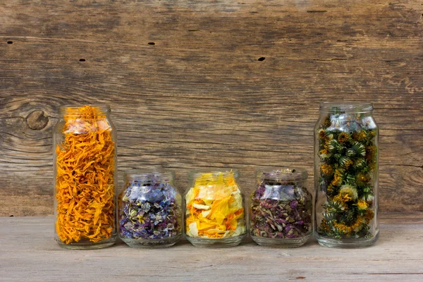 Herbs and flower petals in glass jars on the background of the old wooden barn boards. with space for text. the concept of aromatherapy, homeopathy, alternative medicine