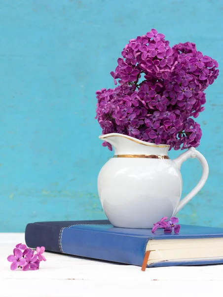 A bouquet of lilac purple flowers in a white vase and the fallen petals on a notepad diary on a blue background