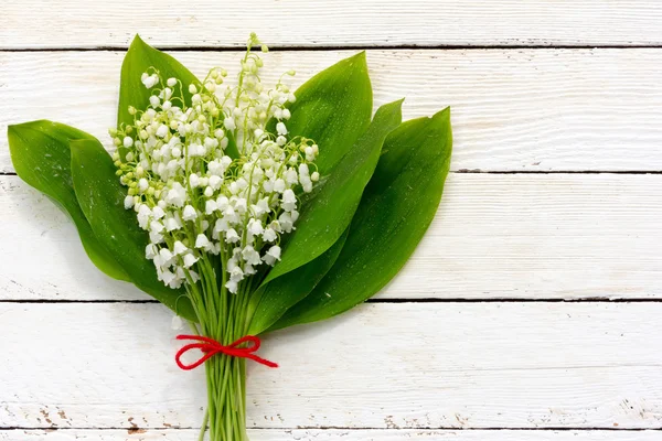 Bouquet of lilies of the valley flowers with green leaves tied with a red rope in the water droplets on the white wooden boards. with space for posting information