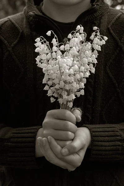 Village boy in knit sweater with a bouquet of lilies of the valley white flowers in her hands. selective focus. black and white photo