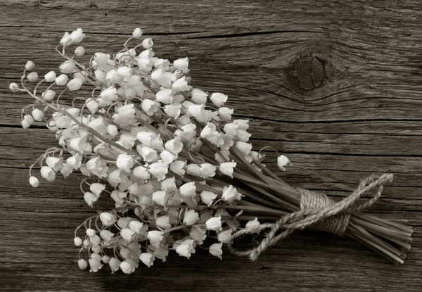 Lily of the valley bouquet of white flowers tied with string on a background of old gray barn boards in the cracks close up